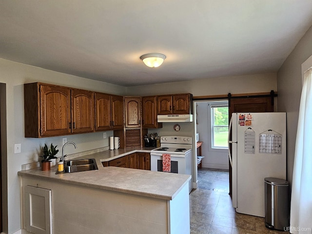 kitchen with white appliances, under cabinet range hood, light countertops, a sink, and a peninsula