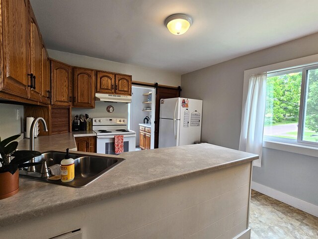 kitchen with white appliances, brown cabinetry, under cabinet range hood, a sink, and a peninsula