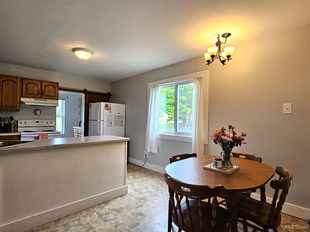 kitchen featuring a barn door, baseboards, under cabinet range hood, white appliances, and a notable chandelier