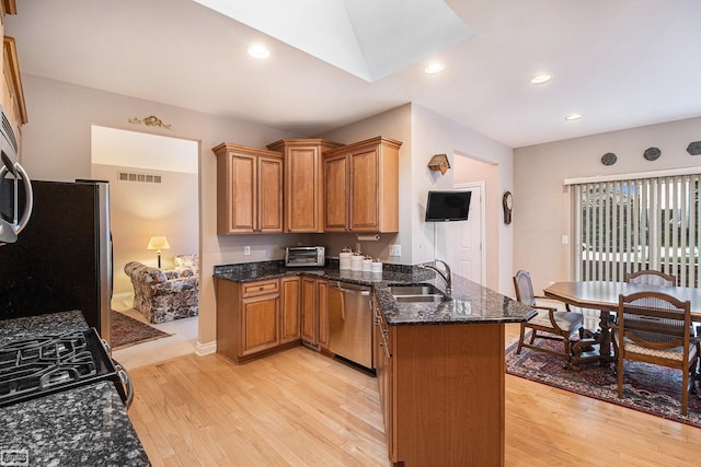 kitchen featuring visible vents, a peninsula, a sink, light wood finished floors, and stainless steel appliances