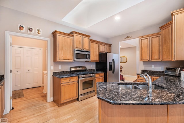kitchen featuring light wood-style floors, a sink, dark stone countertops, and appliances with stainless steel finishes
