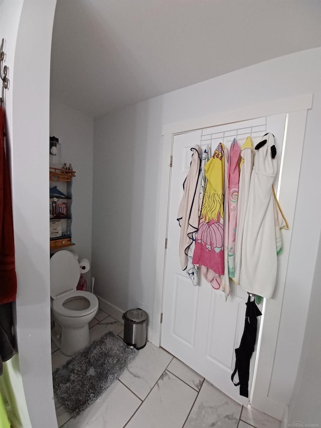 bathroom featuring toilet, marble finish floor, and baseboards
