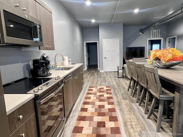kitchen with a sink, stainless steel appliances, light wood-style floors, visible vents, and light countertops