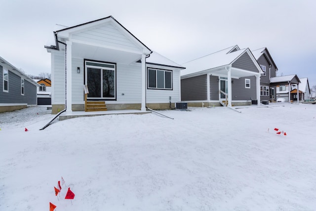 snow covered rear of property featuring entry steps and central AC unit