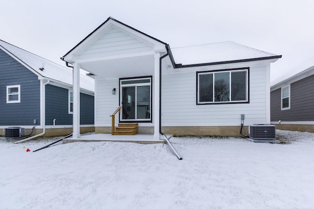 snow covered back of property with entry steps and central AC unit