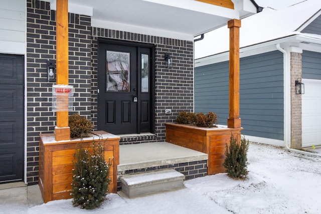 snow covered property entrance with covered porch and brick siding
