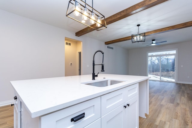 kitchen with light wood-style flooring, beamed ceiling, a sink, open floor plan, and a kitchen island with sink