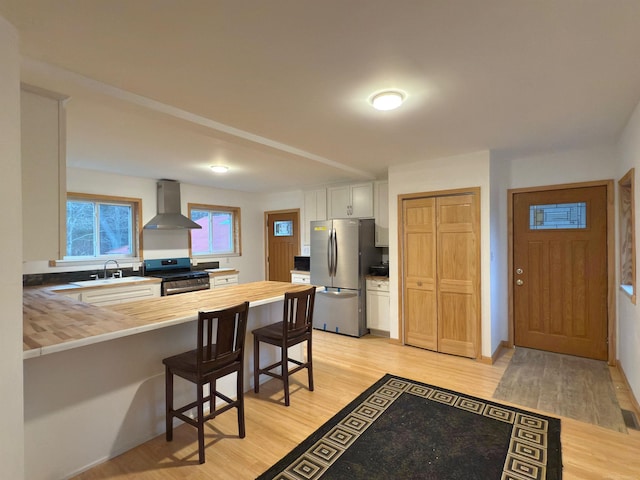 4358 Lakeshore Rd, Lexington, MI 48450 - kitchen with wall chimney range hood, wood counters, a sink, stainless steel appliances, and a peninsula