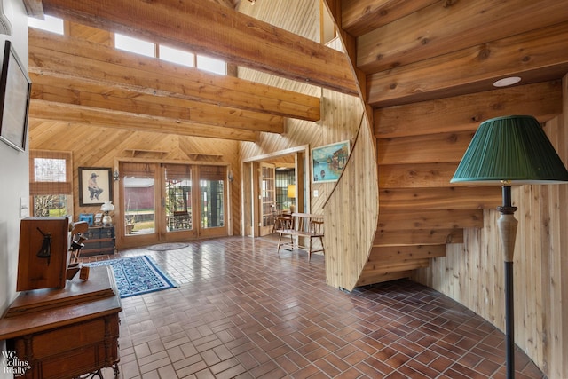 interior space featuring beam ceiling, wood walls, brick floor, and stairway
