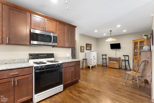 kitchen featuring recessed lighting, light stone countertops, stainless steel microwave, gas range oven, and dark wood-style floors