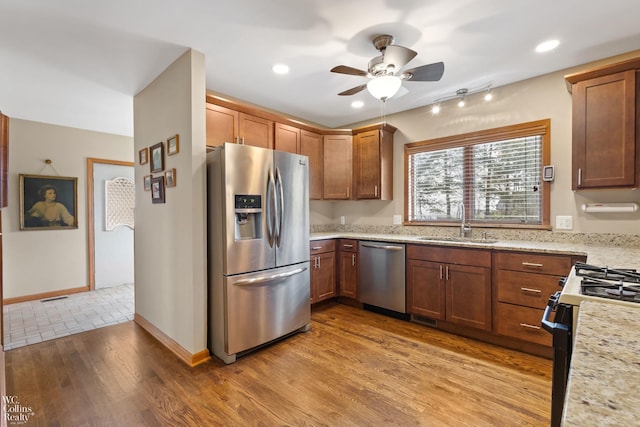 kitchen featuring a sink, ceiling fan, light wood-type flooring, light stone counters, and appliances with stainless steel finishes