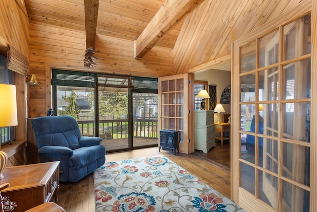 living area featuring beamed ceiling, a wood stove, wood walls, wood ceiling, and hardwood / wood-style flooring