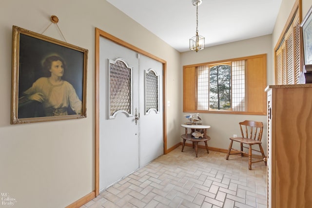 interior space featuring an inviting chandelier, brick patterned floor, and baseboards