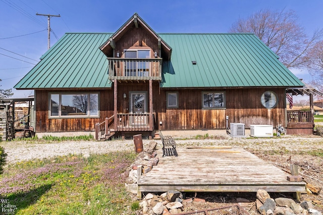 back of property with cooling unit, a standing seam roof, metal roof, and a wooden deck