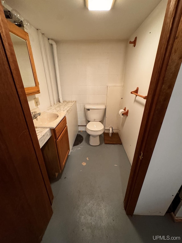 bathroom with toilet, concrete floors, concrete block wall, and vanity