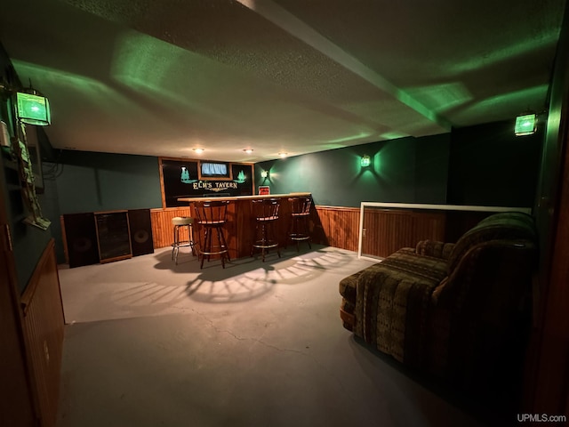 bar with concrete floors, bar, a wainscoted wall, and a textured ceiling