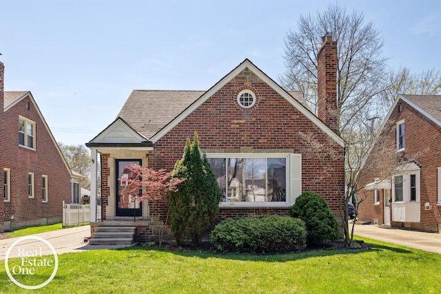 tudor-style house featuring a chimney, brick siding, and a front yard
