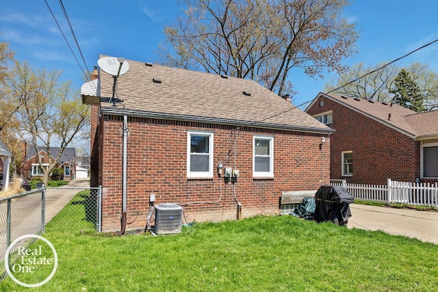 back of property with fence, cooling unit, a shingled roof, and brick siding