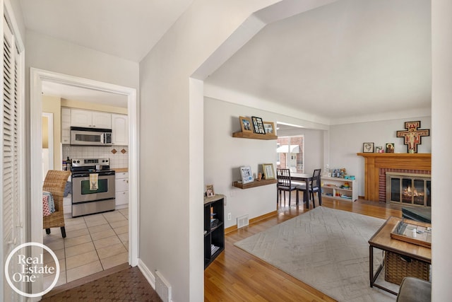 living area featuring a brick fireplace, light wood finished floors, visible vents, and baseboards