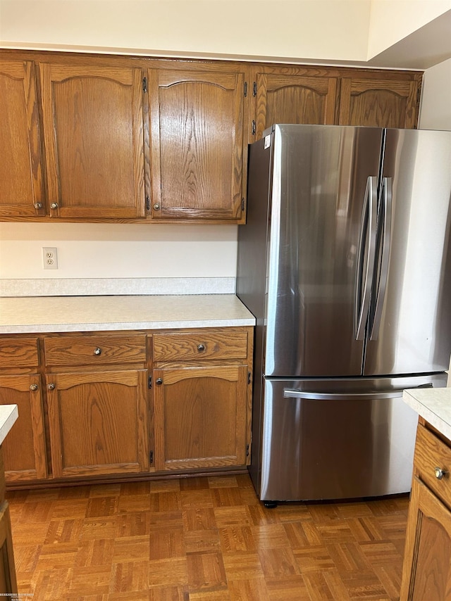 kitchen featuring light countertops, freestanding refrigerator, and brown cabinetry
