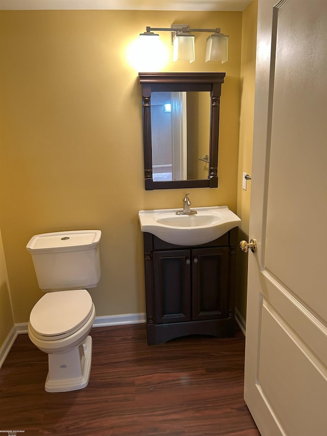 half bathroom with baseboards, vanity, toilet, and wood finished floors