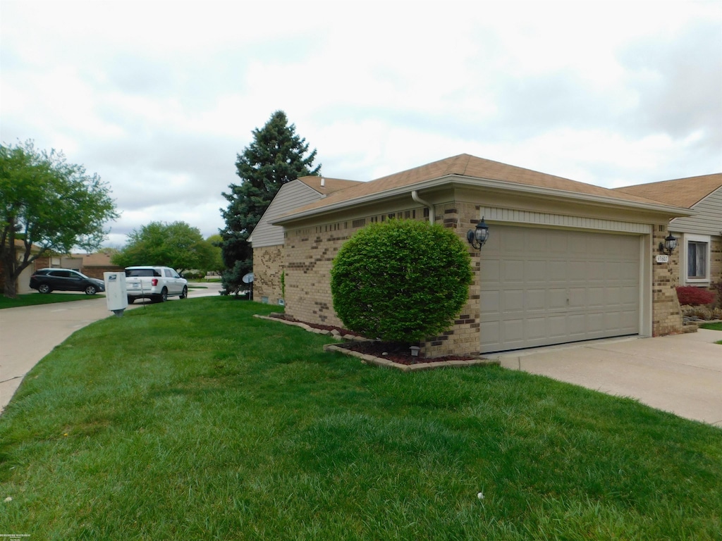 view of side of home featuring driveway, a yard, an attached garage, and brick siding