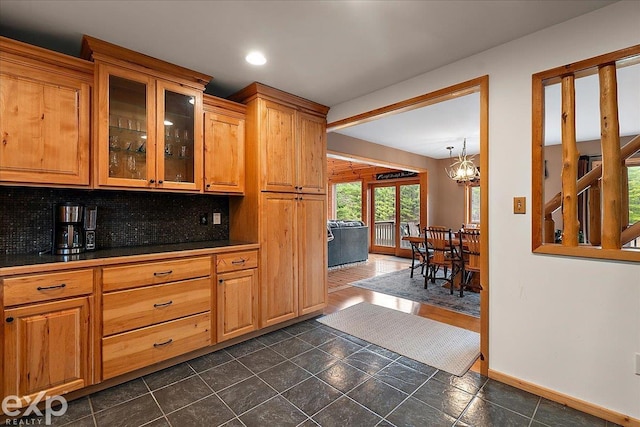 kitchen featuring glass insert cabinets, dark countertops, a chandelier, baseboards, and backsplash
