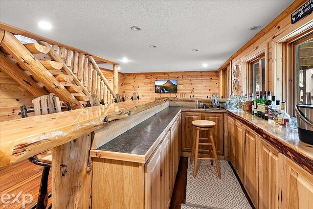 bar with wet bar, recessed lighting, a textured ceiling, and wood walls