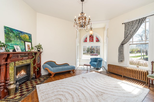 living area featuring radiator, a notable chandelier, a tiled fireplace, and wood finished floors