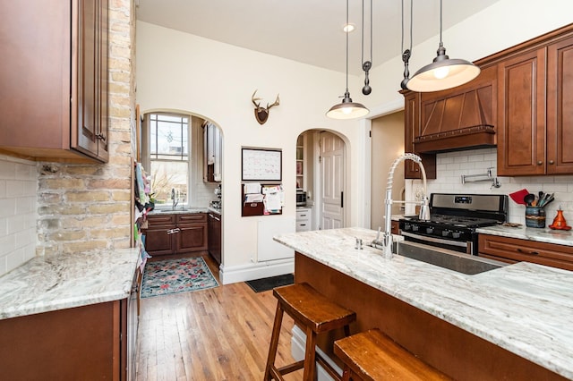 kitchen with a breakfast bar area, decorative backsplash, hardwood / wood-style floors, arched walkways, and stainless steel gas range oven
