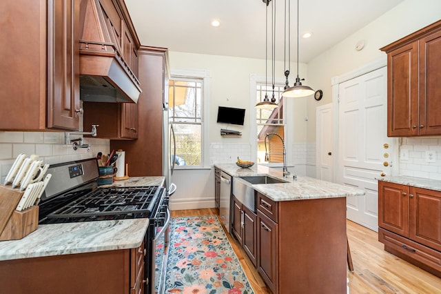 kitchen with tasteful backsplash, a sink, appliances with stainless steel finishes, light wood-style floors, and premium range hood