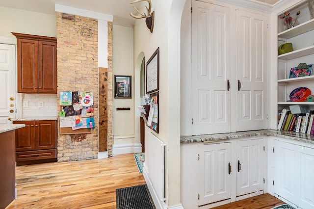 kitchen featuring light stone countertops, arched walkways, brown cabinetry, open shelves, and light wood-type flooring