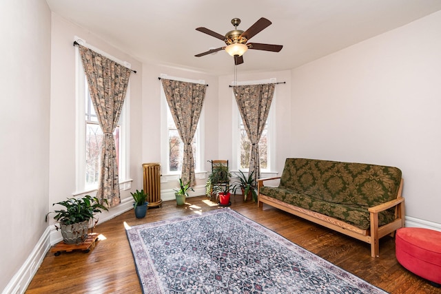 living area featuring baseboards, hardwood / wood-style flooring, a ceiling fan, and plenty of natural light