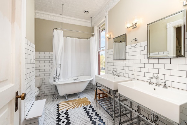 full bath featuring a freestanding bath, tile walls, toilet, a sink, and crown molding