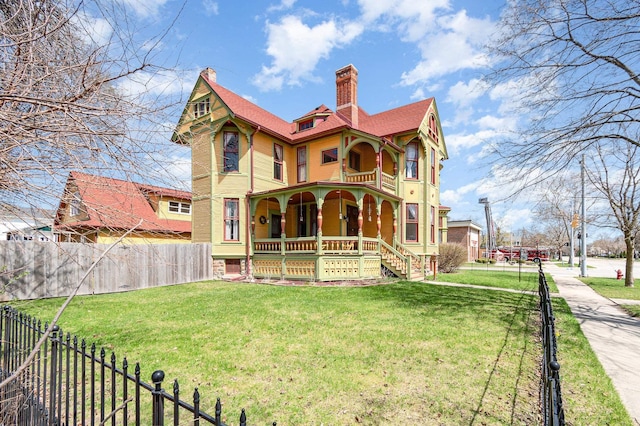 view of front facade with a front lawn, a chimney, covered porch, and fence