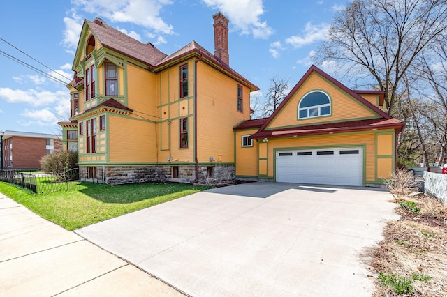 victorian home with driveway, a chimney, fence, a front lawn, and a garage