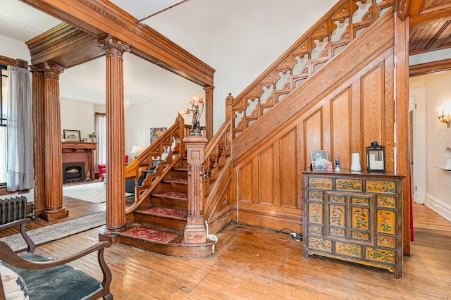 stairs with a fireplace, ornate columns, wood finished floors, and radiator heating unit