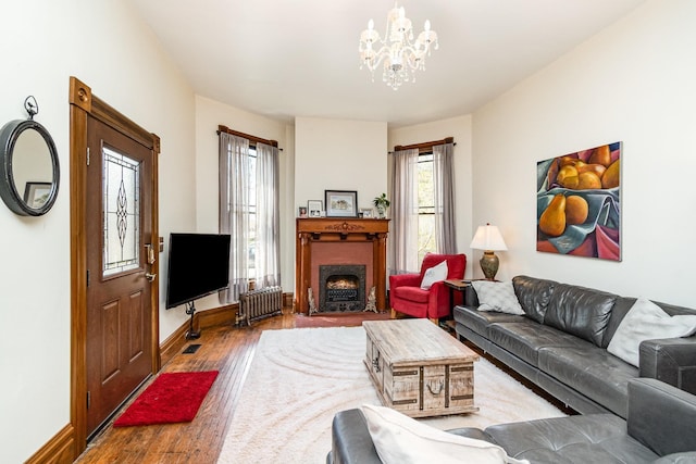 living area featuring a fireplace with flush hearth, a notable chandelier, radiator heating unit, baseboards, and wood finished floors