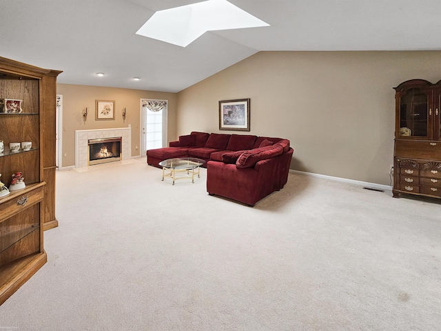 carpeted living area with a tile fireplace, visible vents, vaulted ceiling with skylight, and baseboards