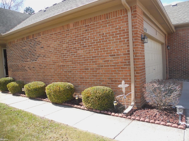 view of property exterior with roof with shingles, an attached garage, and brick siding
