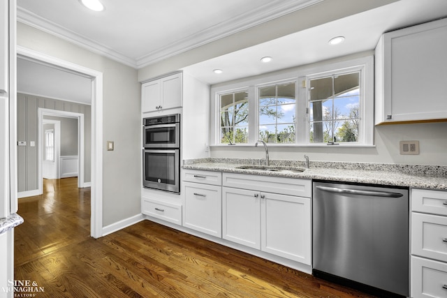kitchen featuring appliances with stainless steel finishes, white cabinets, ornamental molding, a sink, and dark wood-style floors