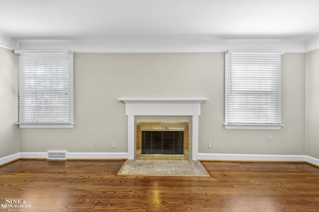unfurnished living room featuring a tiled fireplace, visible vents, wood finished floors, and a wealth of natural light