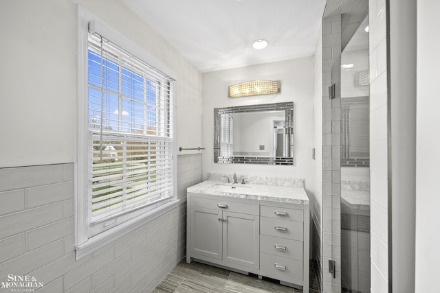 full bath featuring tile walls, tiled shower, and vanity