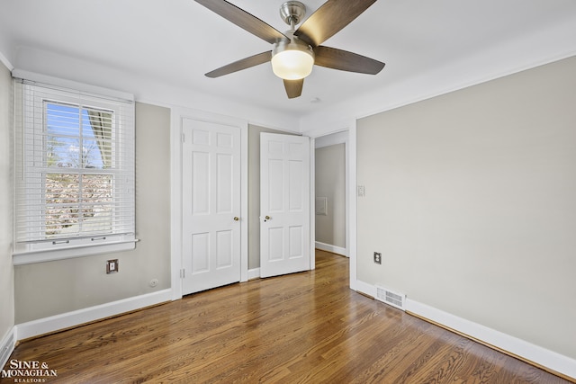 unfurnished bedroom featuring a ceiling fan, visible vents, wood finished floors, and baseboards