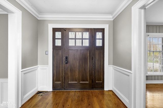 entryway featuring wood finished floors, crown molding, a decorative wall, and wainscoting