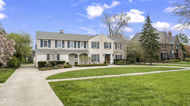 view of front of property featuring a chimney, a front yard, brick siding, and curved driveway