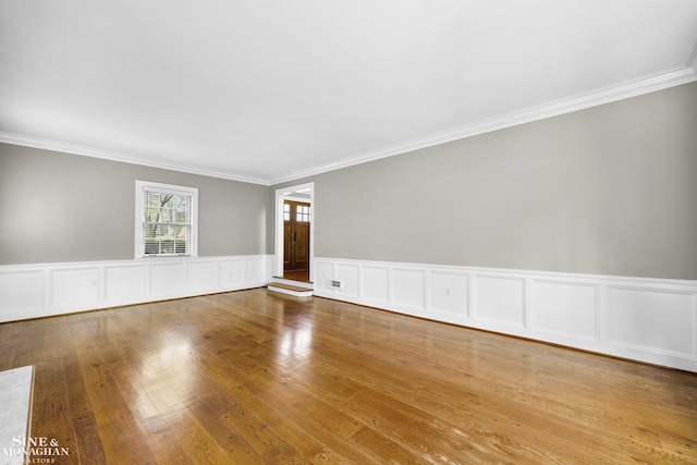 empty room featuring wood finished floors, crown molding, and wainscoting