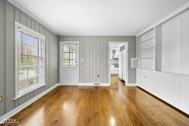 unfurnished living room featuring wood finished floors, visible vents, ornamental molding, and baseboards