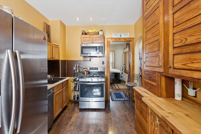 kitchen with tasteful backsplash, a sink, stainless steel appliances, dark wood-style flooring, and butcher block countertops