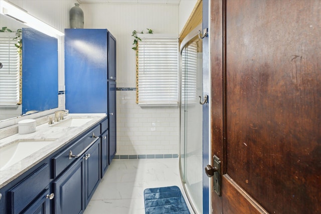 full bathroom featuring a stall shower, marble finish floor, double vanity, and a sink